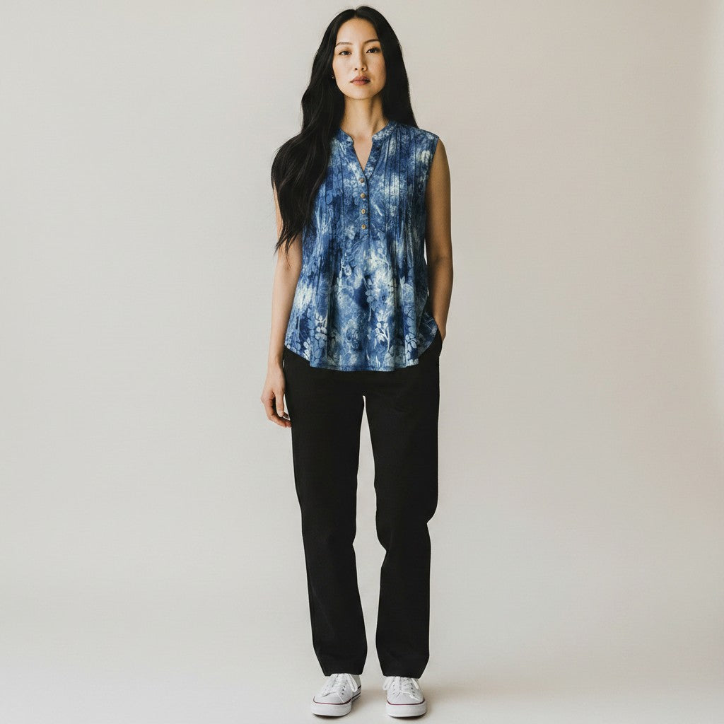 A woman with a floral blue shirt, black skinny jeans and black high heels on a studio gray background.