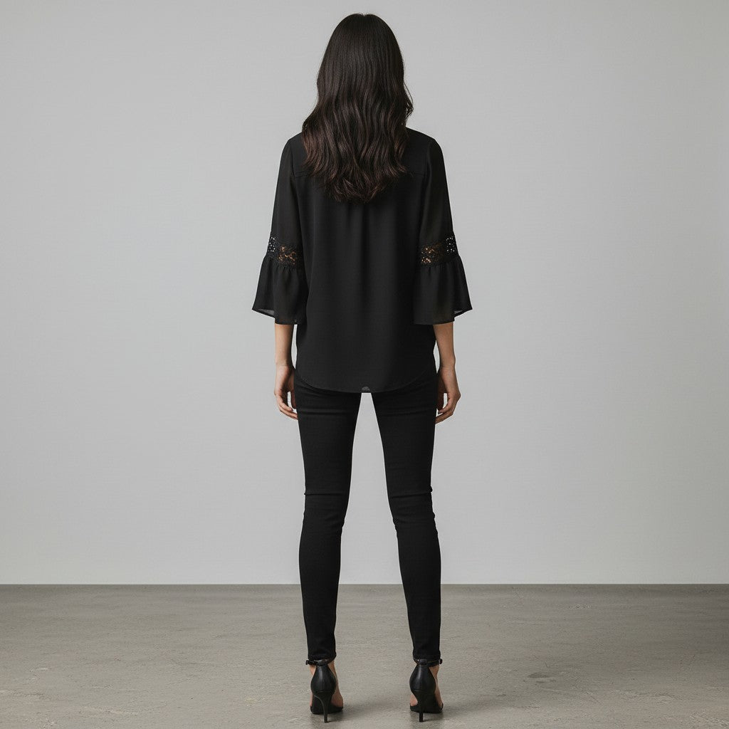 A woman wearing a black blouse, black jeans and black high heels on a studio gray background.