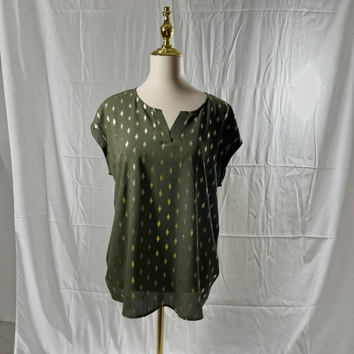 A woman wearing a green and gold shirt with black jeans, black heels on a studio gray background. 