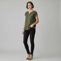A woman wearing a green and gold shirt with black jeans, black heels on a studio gray background. 