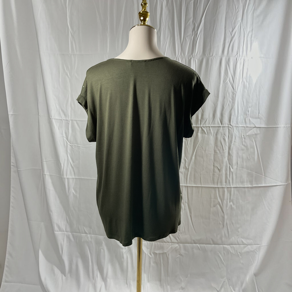 A woman wearing a green and gold shirt with black jeans, black heels on a studio gray background. 