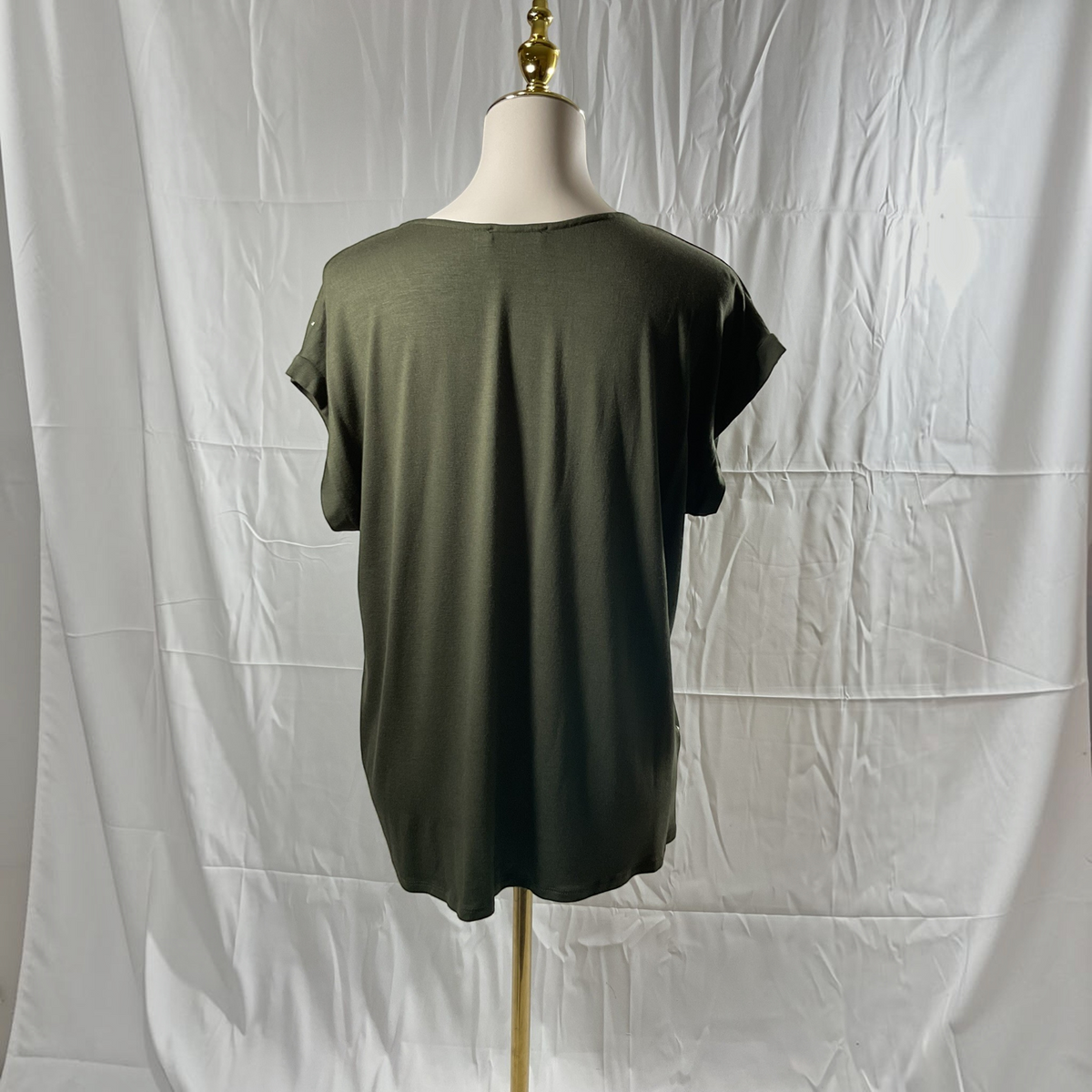 A woman wearing a green and gold shirt with black jeans, black heels on a studio gray background. 