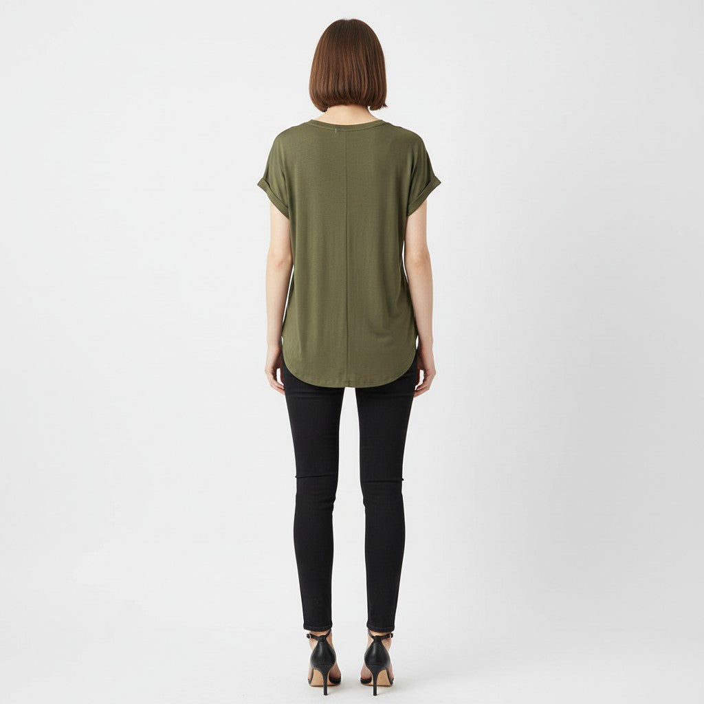 A woman wearing a green and gold shirt with black jeans, black heels on a studio gray background. 