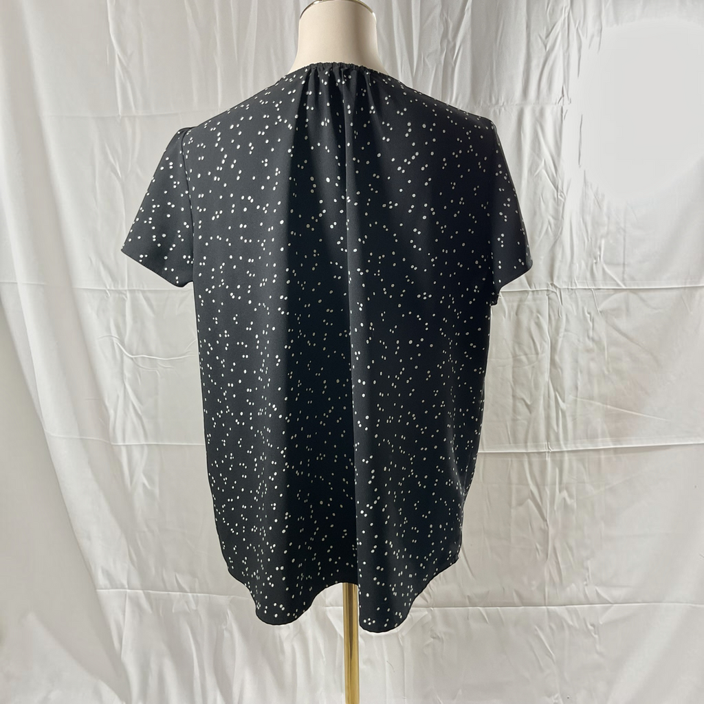 A woman with a black and white dot shirt, black skinny jeans, black high heels on a studio gray background.