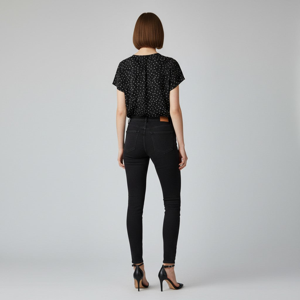 A woman with a black and white dot shirt, black skinny jeans, black high heels on a studio gray background.