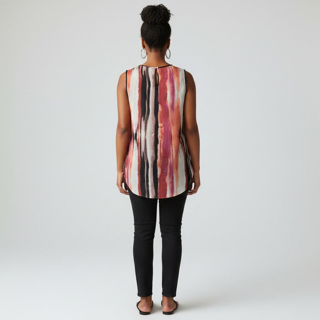A woman viewed from the back wearing a sleeveless top with vertical abstract stripes in pink, red, black, and off-white, paired with black pants and sandals, against a light gray studio background.