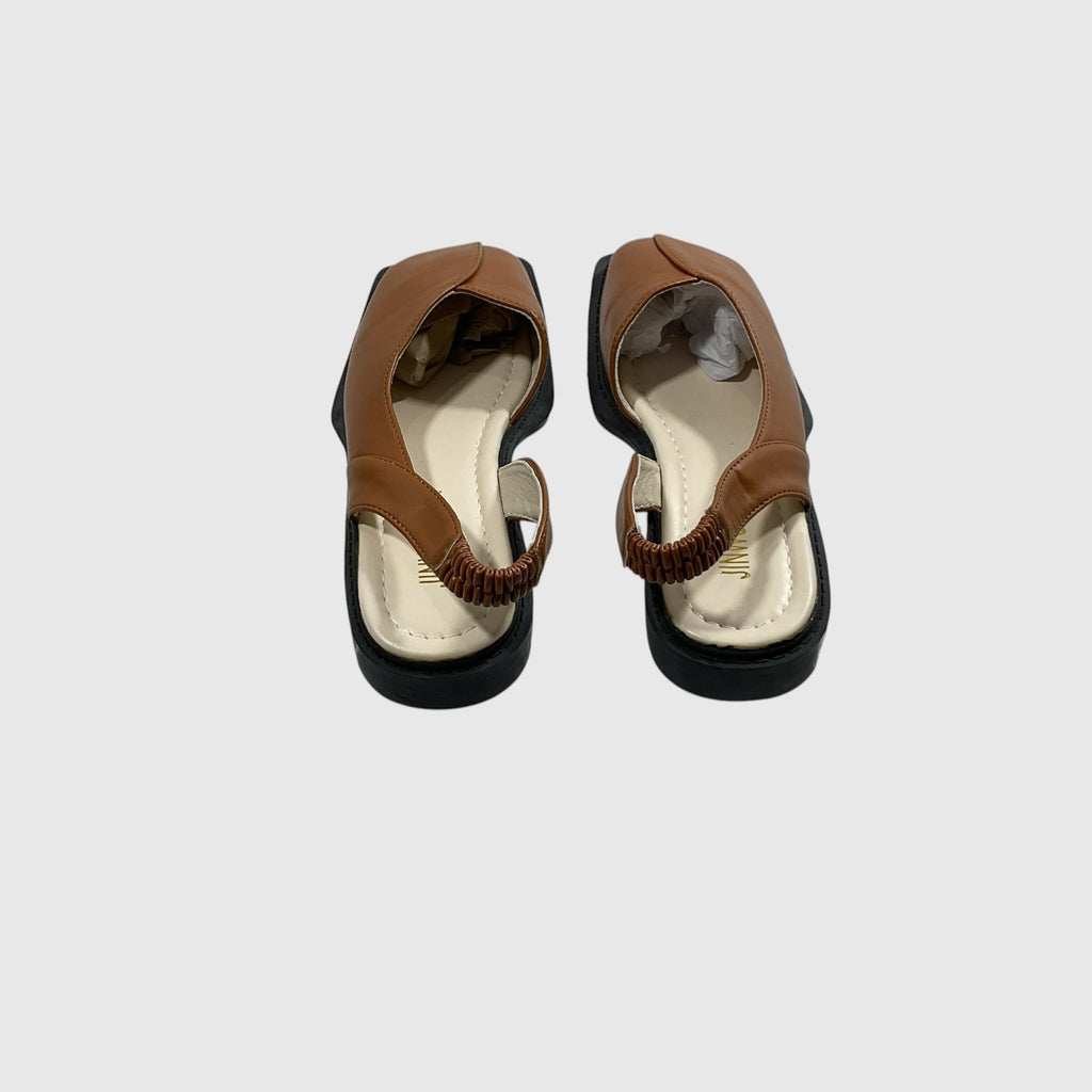 A pair of women's flat sandals shown from a top-down view, featuring tan leather straps with a braided detail, a cream-colored insole, and black soles, set against a plain light gray background.