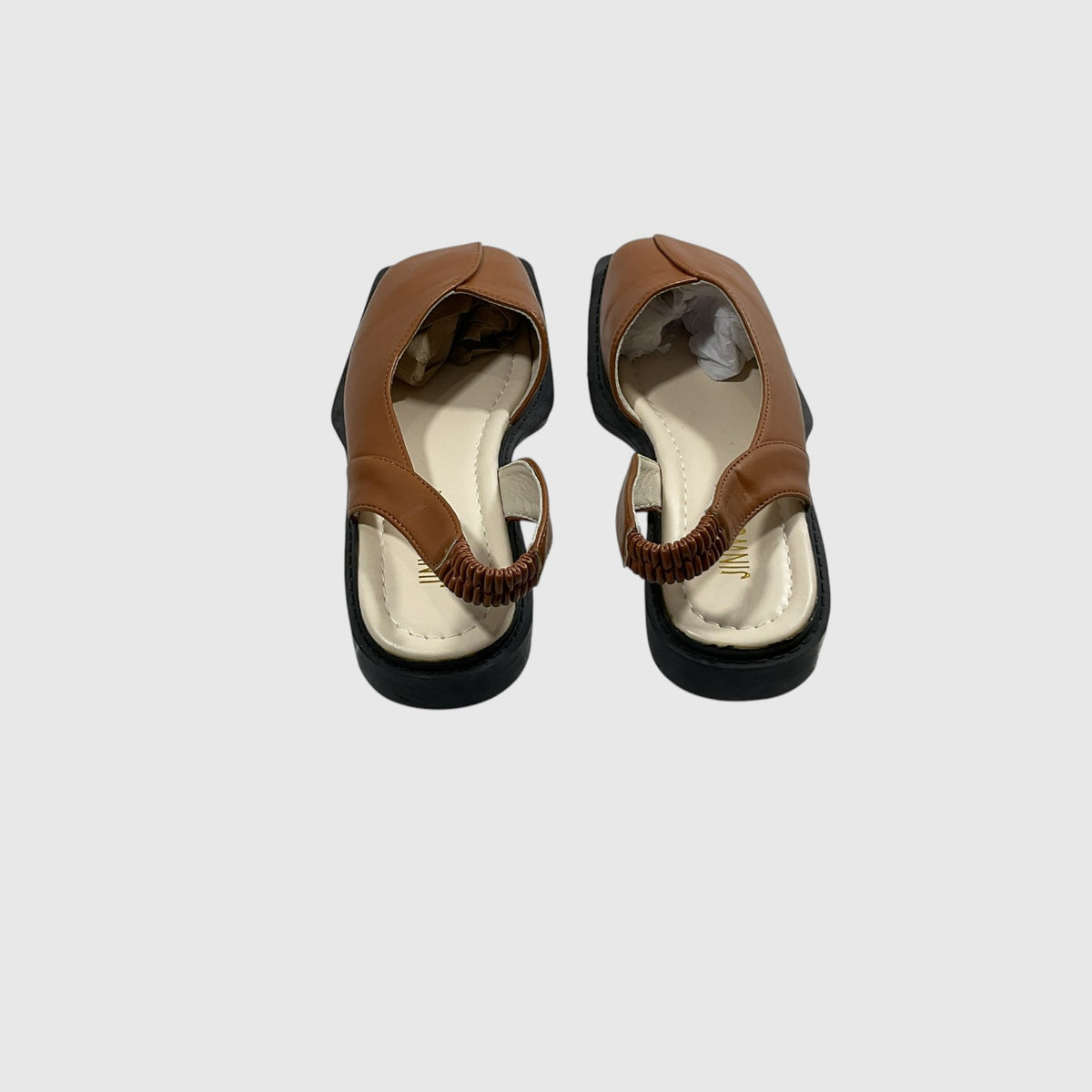 A pair of women's flat sandals shown from a top-down view, featuring tan leather straps with a braided detail, a cream-colored insole, and black soles, set against a plain light gray background.