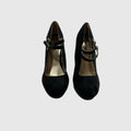 A pair of black suede Mary Jane pumps with gold-tone buckle straps, shown from a top-down view on a light gray background.