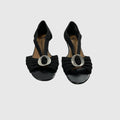 A pair of black slingback wedge sandals with a wide front strap featuring a large silver-tone circular buckle, shown against a light gray background.