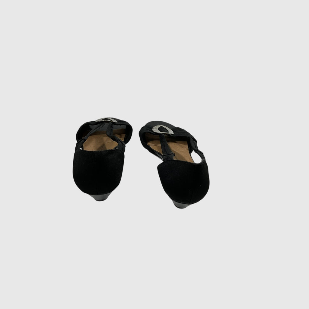 A pair of black wedge shoes with cutout straps and a small circular silver emblem on the toe, shown from a top-down view on a light gray background.