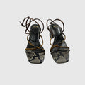 A pair of women's heeled sandals featuring a snakeskin-patterned toe strap, black leather straps, and a thin brown leather wrap-around strap, shown against a light gray background.