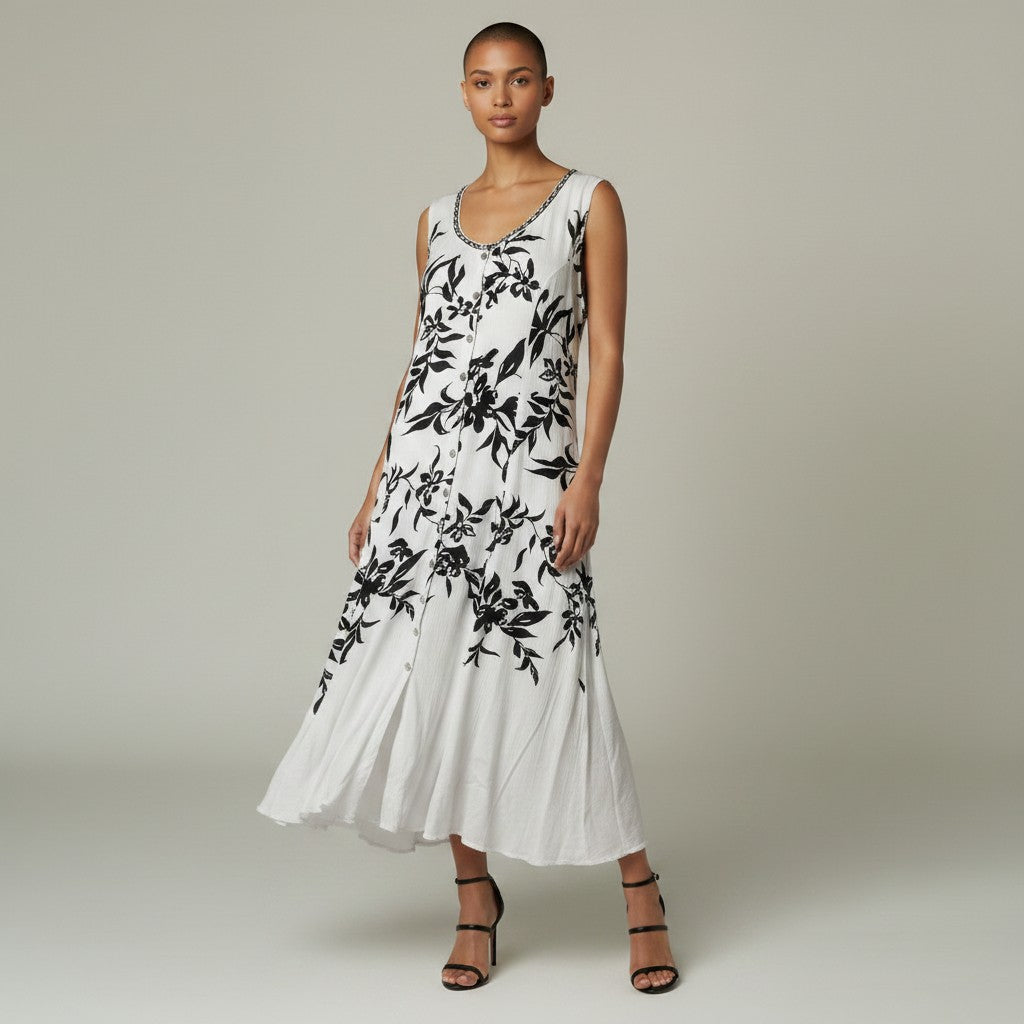 A woman modeling a sleeveless white midi dress with a black floral print, standing against a neutral light gray studio background.