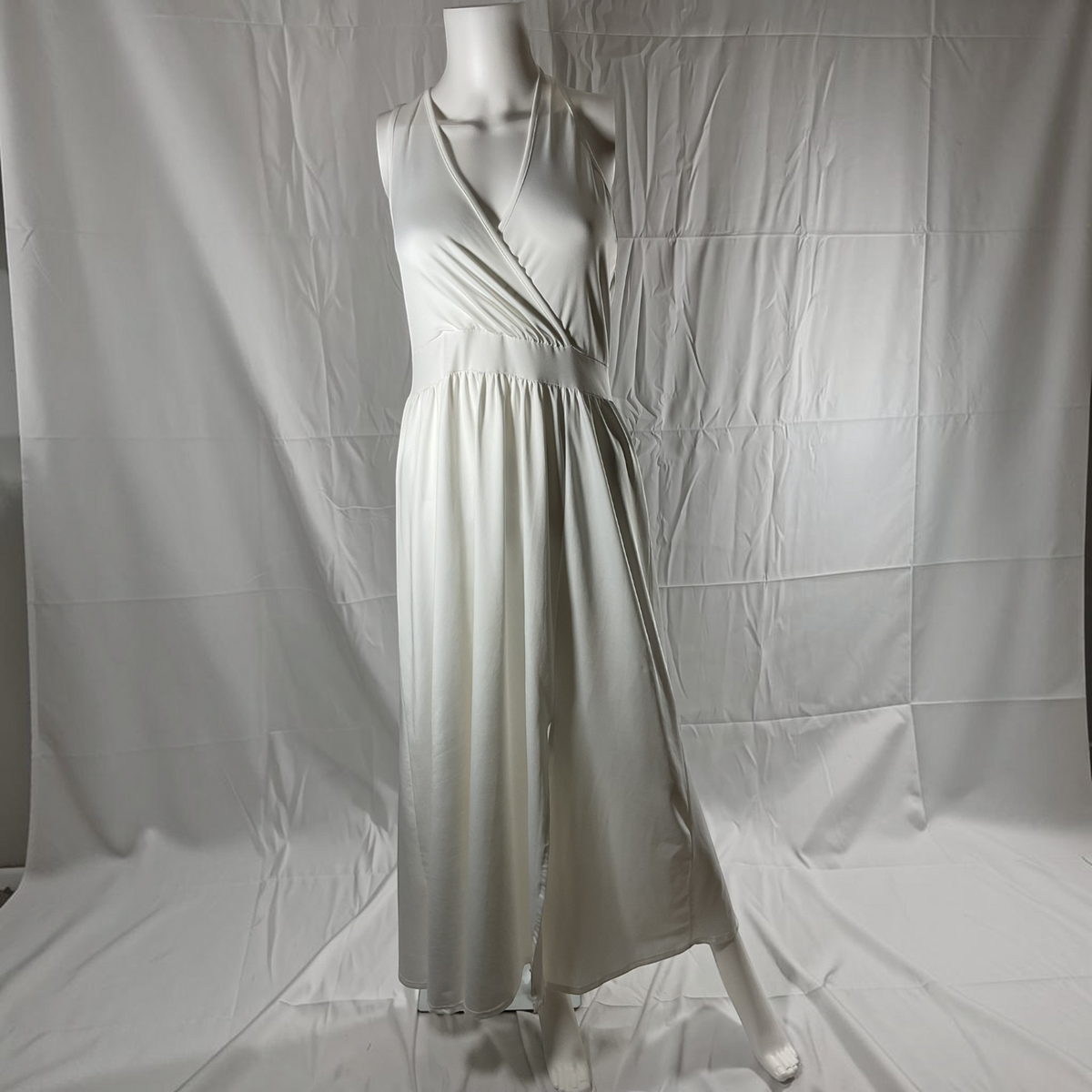 A sleeveless white wrap-style maxi dress displayed on a mannequin against a wrinkled white fabric backdrop.