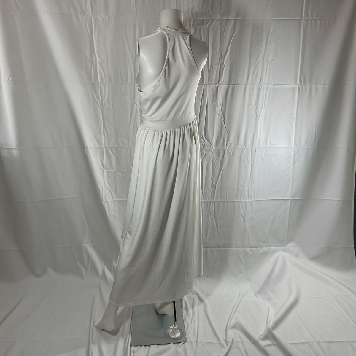 A sleeveless white maxi dress displayed on a white mannequin, photographed against a wrinkled white fabric backdrop.