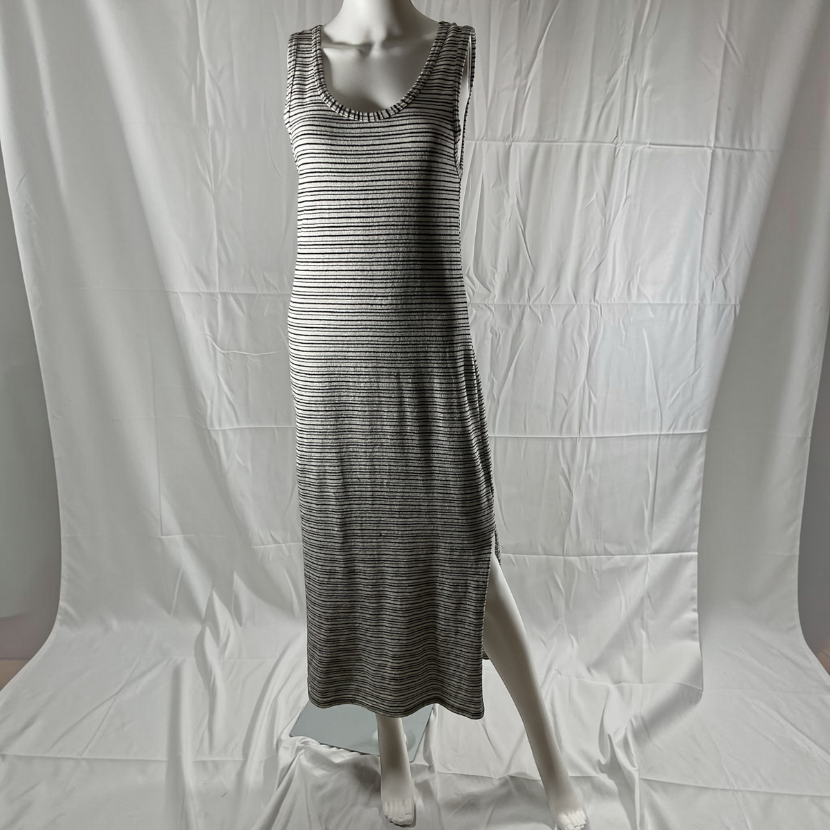 A sleeveless, scoop-neck maxi dress with a fine horizontal stripe pattern in black and white, displayed on a white mannequin against a wrinkled white studio backdrop.