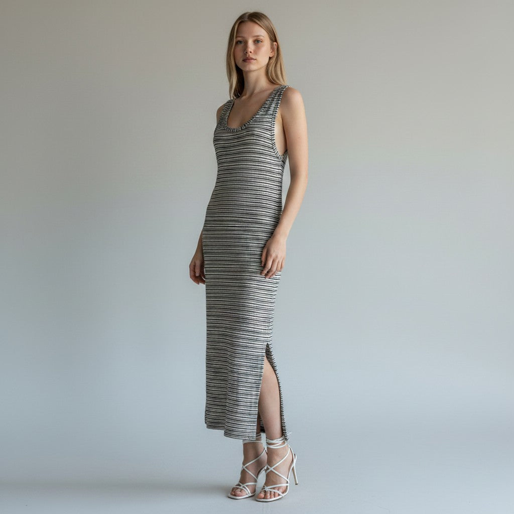 A woman modeling a sleeveless, floor-length striped knit dress with a high side slit, paired with white strappy high-heeled sandals, against a neutral light gray studio background.