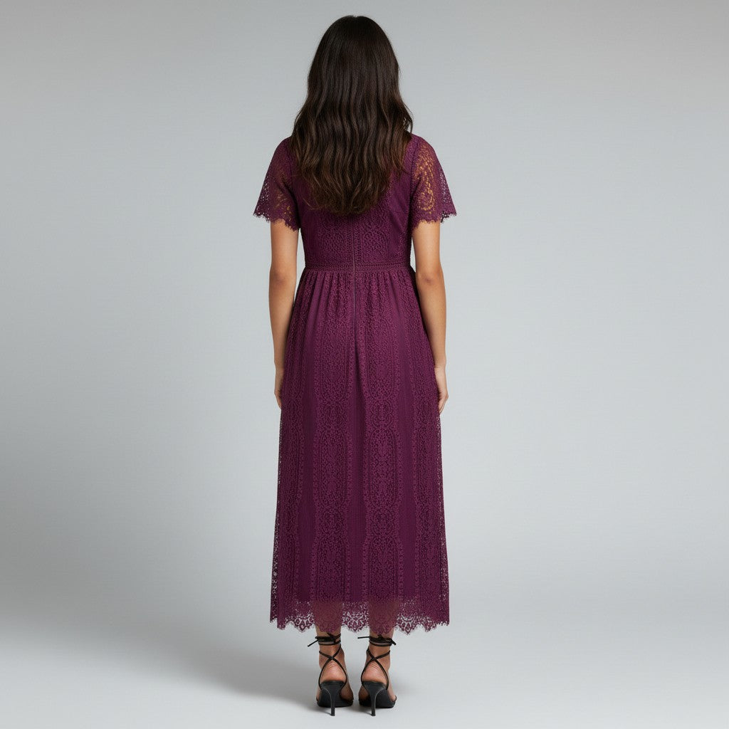 A woman viewed from the back wearing a short-sleeve midi dress in deep burgundy lace, paired with black strappy heels, against a light gray studio background.