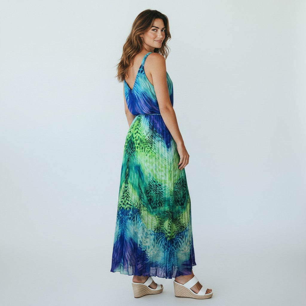 A woman modeling a sleeveless maxi dress with a blue and green tropical leaf print, shown from a three-quarters back view against a light gray studio background.