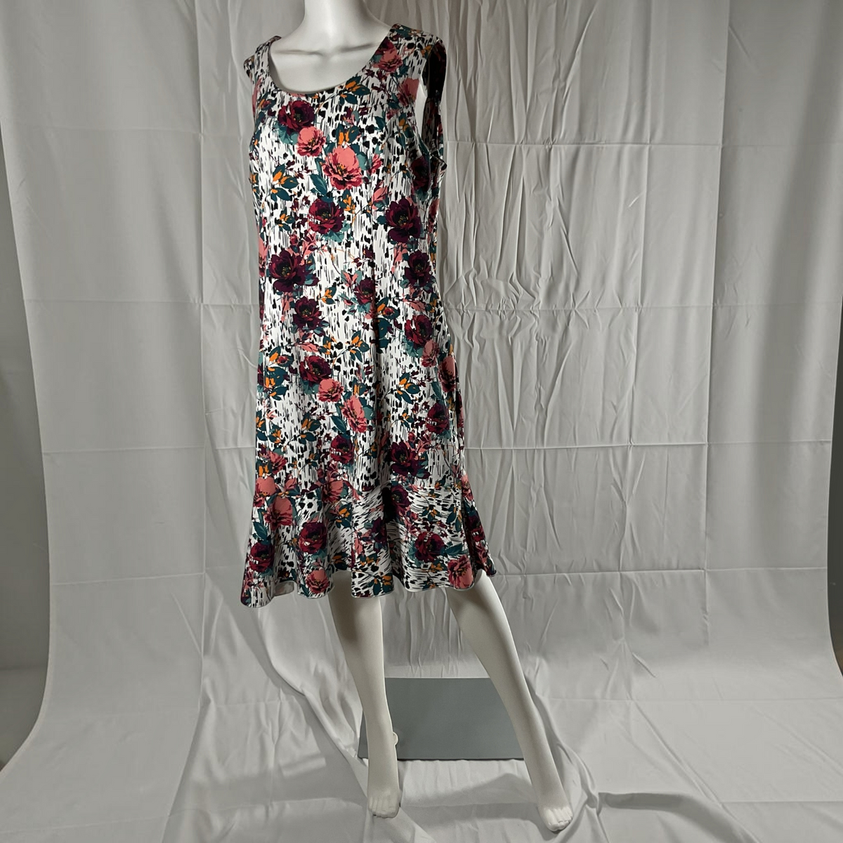 A sleeveless fit-and-flare dress with a vibrant floral print, displayed on a white mannequin against a wrinkled white studio backdrop.