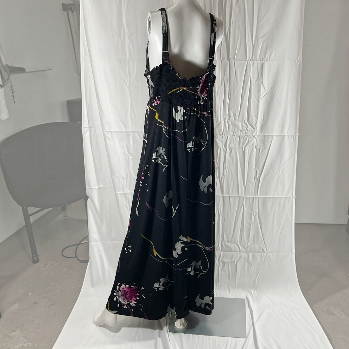 A black midi-length spaghetti-strap dress with a colorful abstract floral and vine print, displayed on a white mannequin against a wrinkled white studio backdrop.