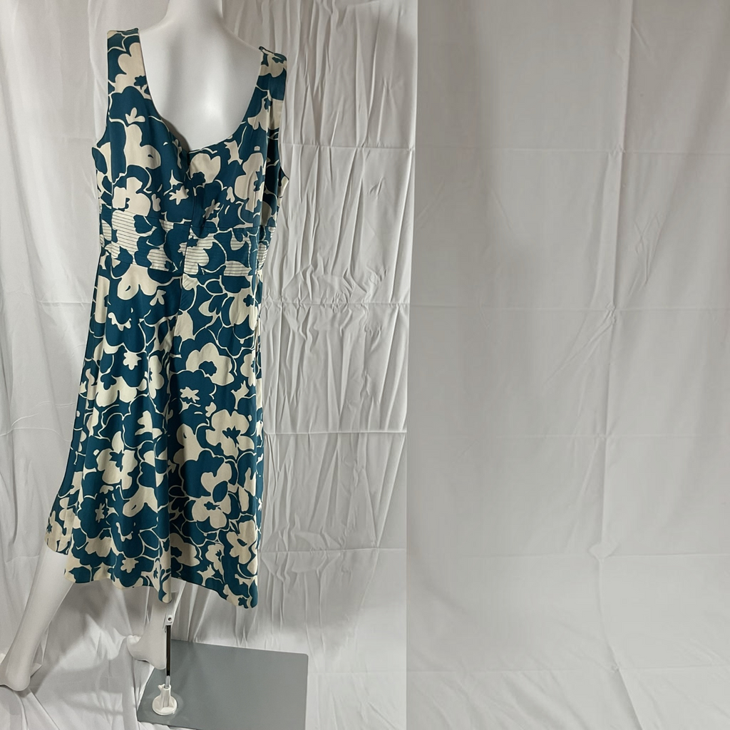 A sleeveless V-neck A-line dress with a blue and cream floral pattern, displayed on a white mannequin against a wrinkled white fabric backdrop.