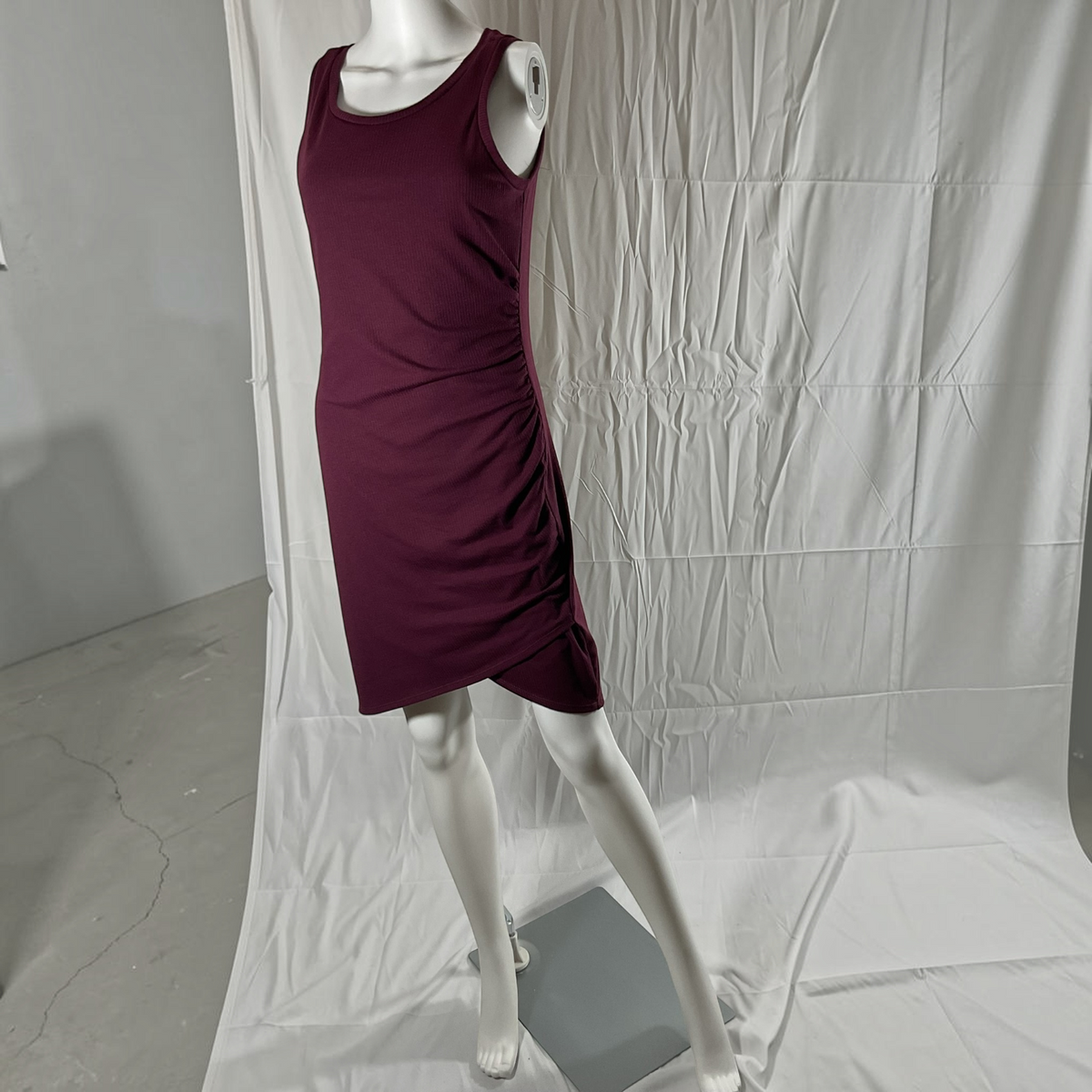 A sleeveless scoop-neck mini dress in deep burgundy, displayed on a white mannequin against a wrinkled white studio backdrop.
