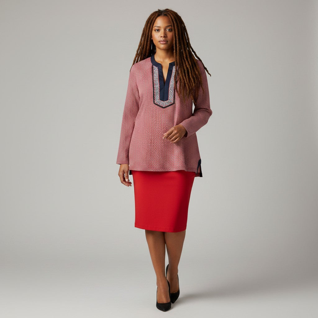 A woman modeling a textured dusty pink long-sleeve tunic top with a navy and silver embroidered V-neckline, paired with a red pencil skirt and black heels, against a neutral gray studio background.