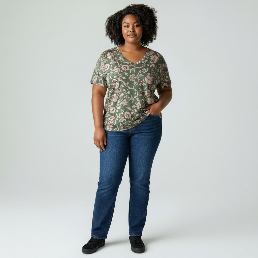A woman modeling a short-sleeve V-neck t-shirt with a green and pink floral pattern, paired with dark blue jeans and black shoes, standing against a light gray studio background.