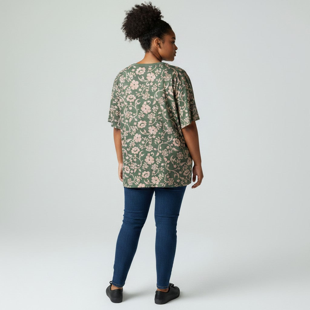 A woman shown from the back wearing a green short-sleeve t-shirt with a pink floral pattern, paired with dark blue skinny jeans and black shoes, against a light gray studio background.