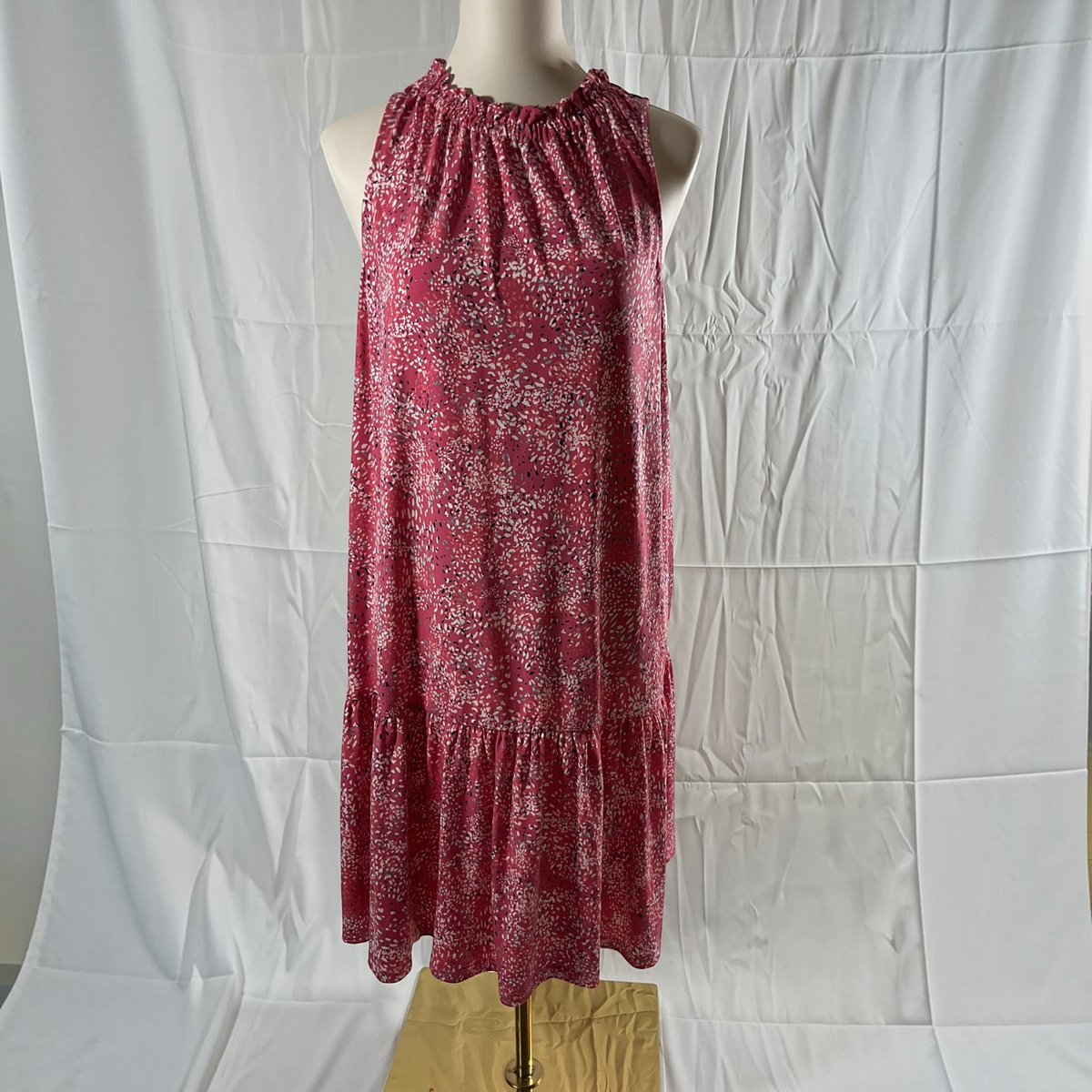 A sleeveless halter-neck dress with a red and white floral pattern, displayed on a mannequin torso against a wrinkled white fabric backdrop.