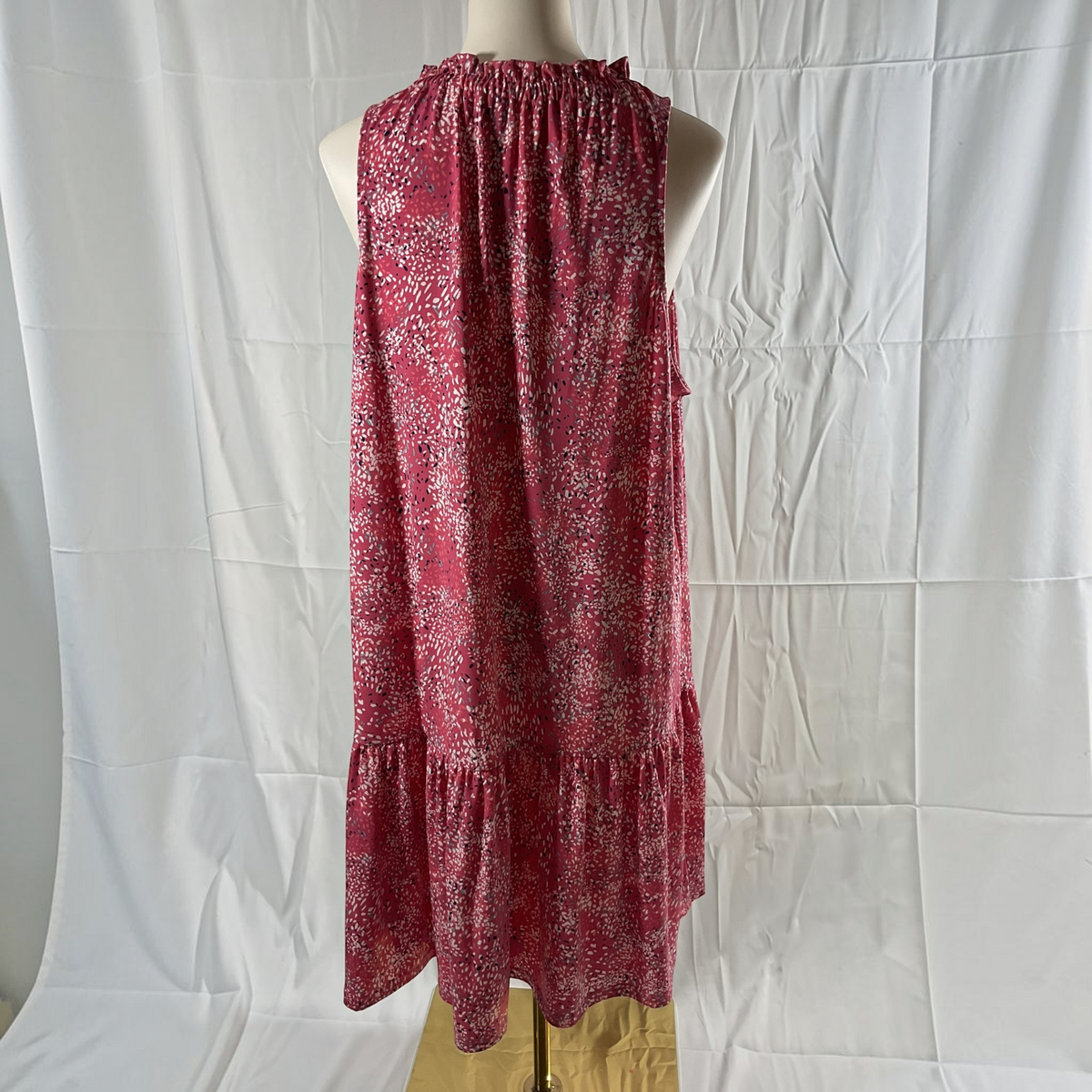 A sleeveless tiered dress with a red and white floral pattern, displayed on a mannequin torso against a white fabric backdrop.
