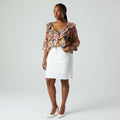 A woman modeling a floral print blouse with ruffled sleeves and a white mini skirt, standing against a light gray studio background.