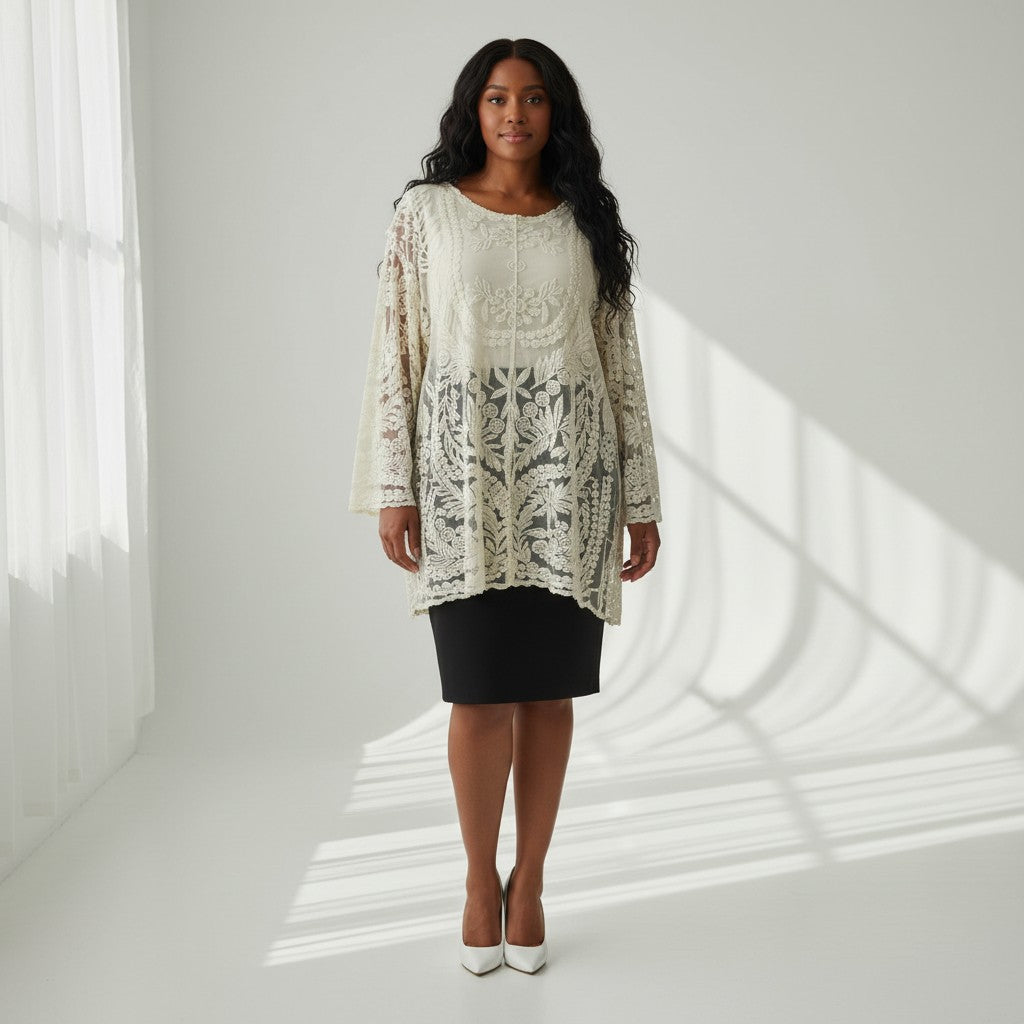 A woman stands in a bright white studio wearing a cream lace tunic top with a black skirt and white heels. The background features soft window shadow patterns cast across the floor and wall.
