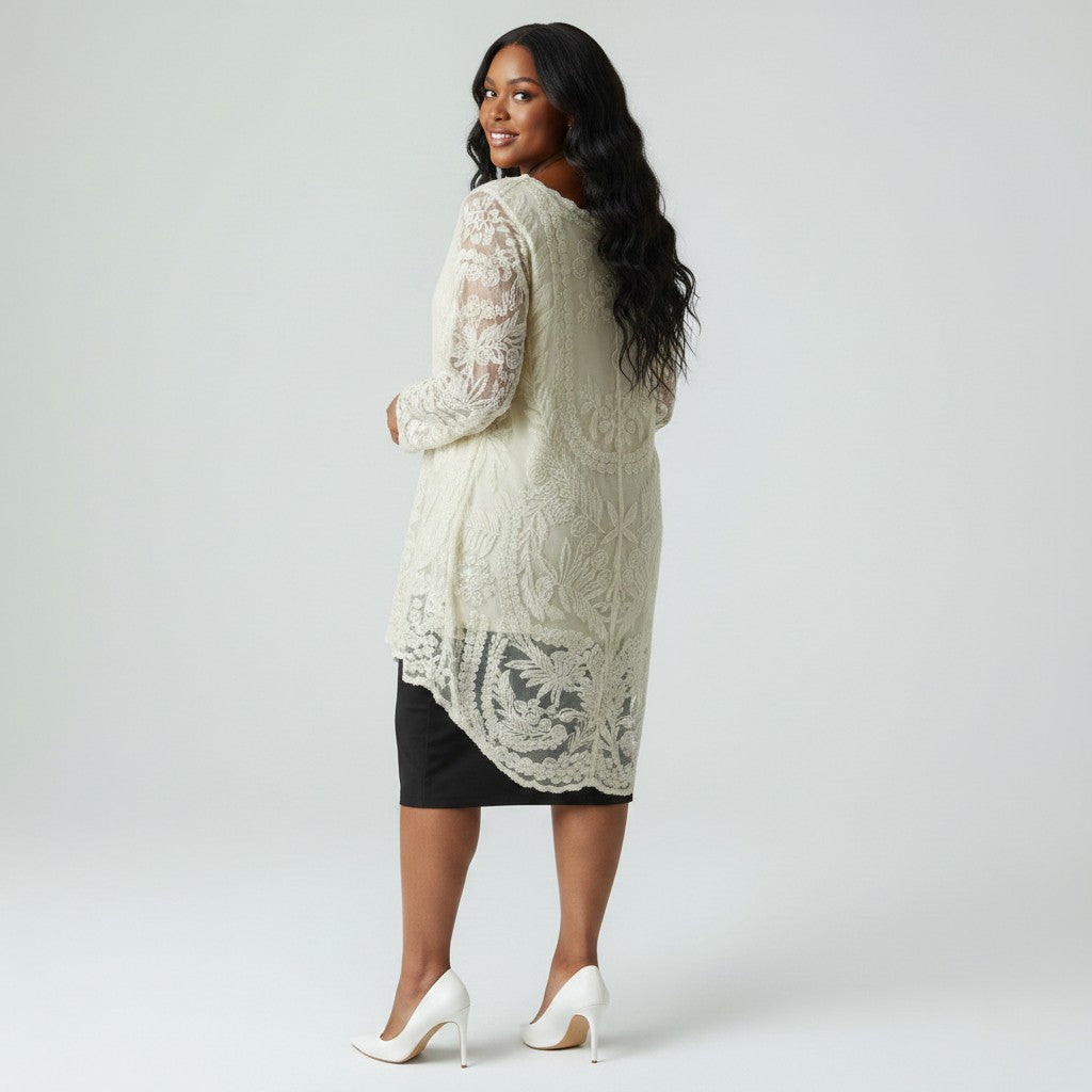 A woman modeling a cream lace long-sleeve tunic cardigan over a black skirt, paired with white heels, photographed against a light gray studio background.