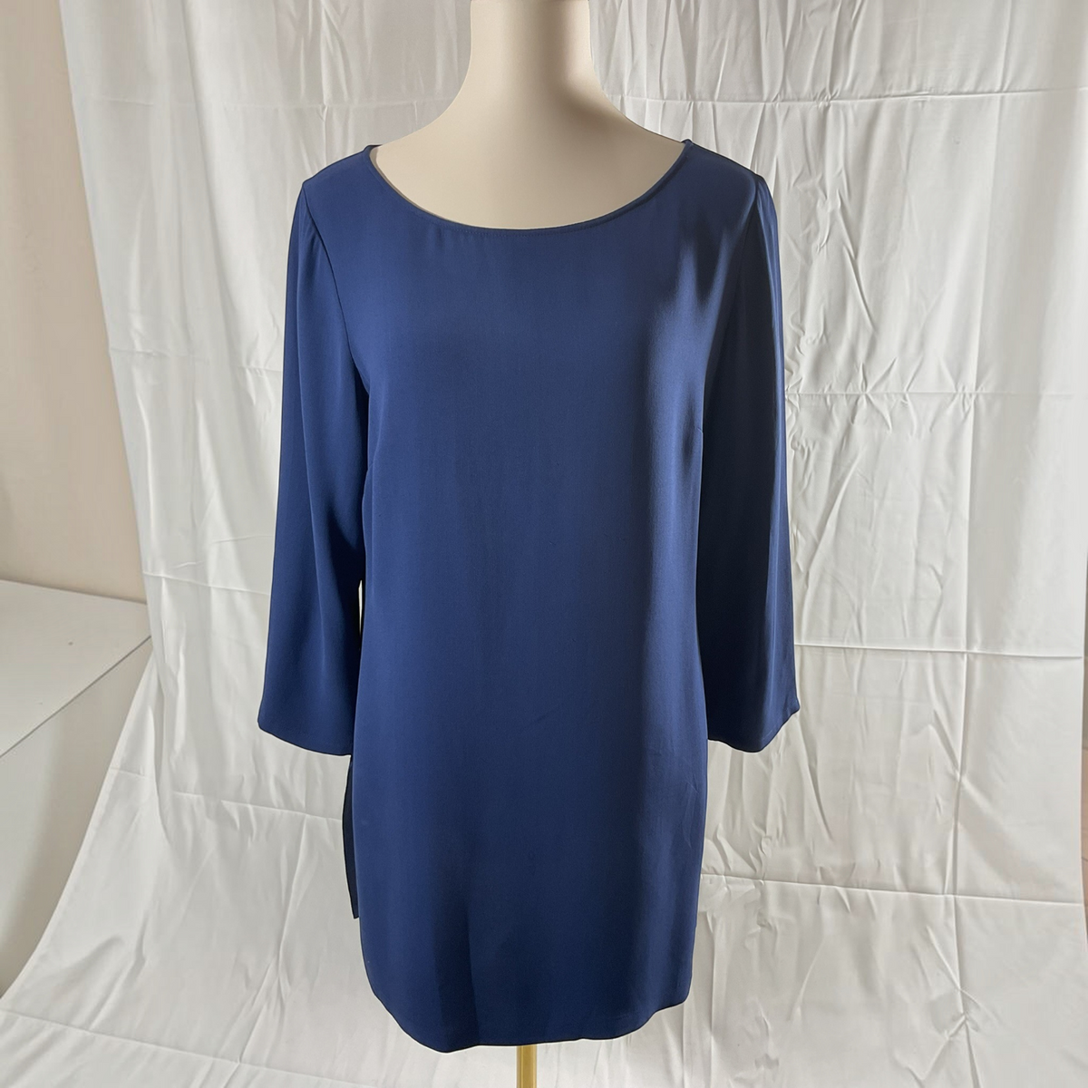 A blue three-quarter sleeve tunic top displayed on a mannequin torso against a white fabric backdrop.