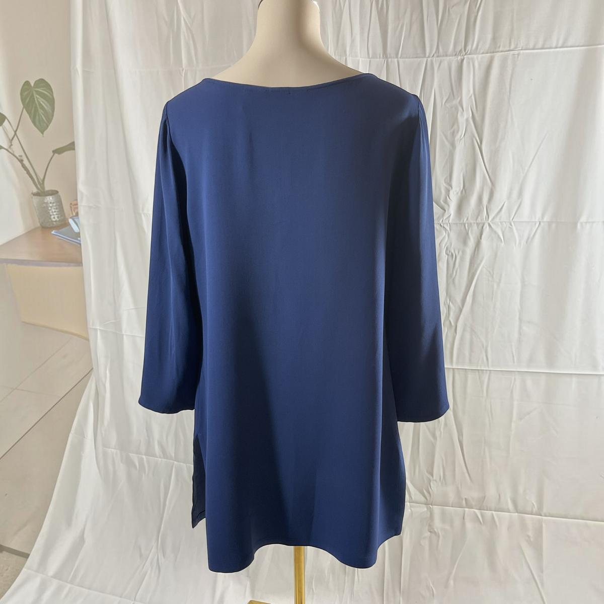 A navy blue long-sleeve tunic top displayed on a mannequin from the back, set against a white fabric backdrop.
