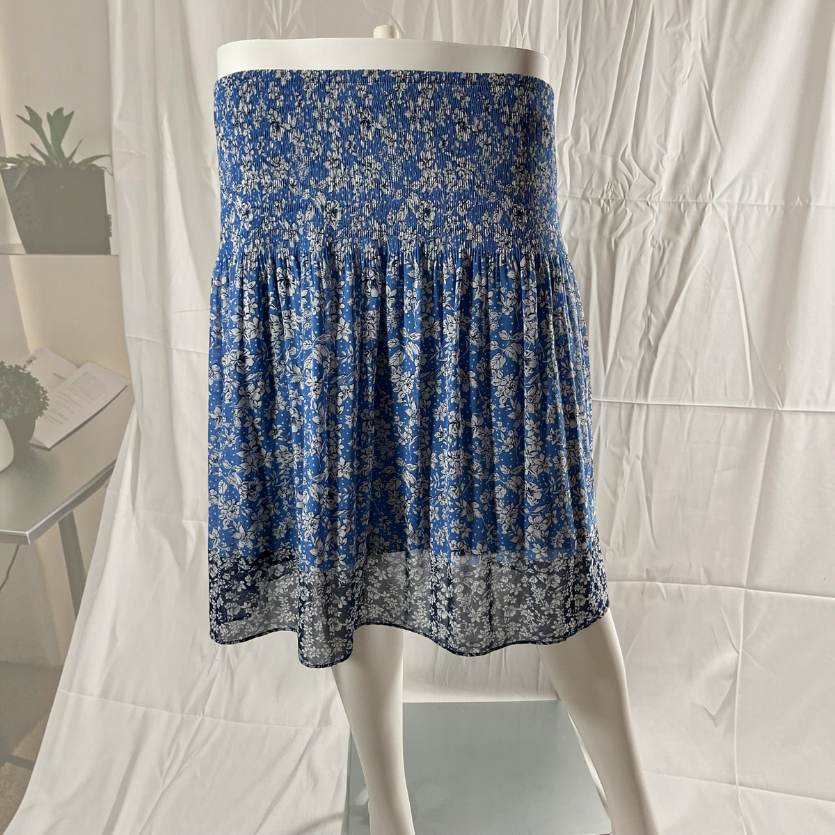 A blue and white floral printed skirt displayed on a white mannequin, set against a wrinkled white fabric backdrop.