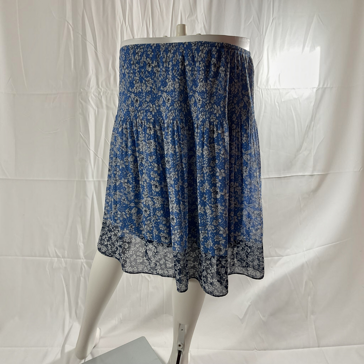 A blue and white floral tiered skirt displayed on a white mannequin against a wrinkled white fabric backdrop.