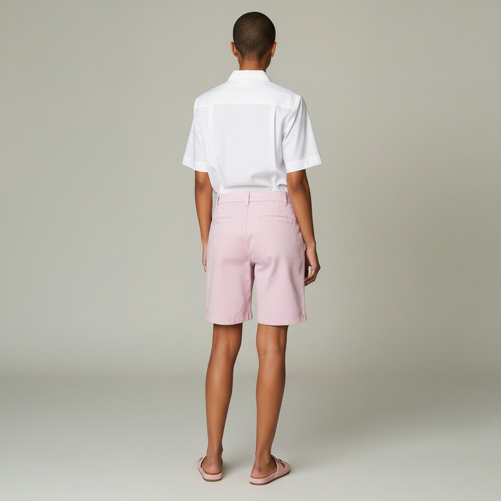 A model shown from the back wearing a white short-sleeve button-up shirt and light pink shorts, standing against a neutral light gray studio background.