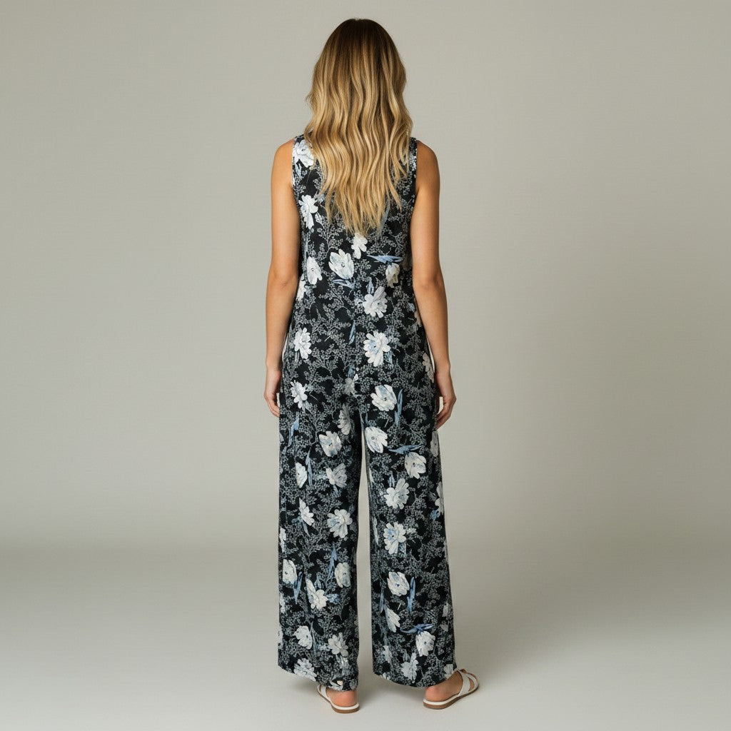 A woman modeling a sleeveless wide-leg jumpsuit with a black base and white floral pattern, standing against a neutral light gray studio background.