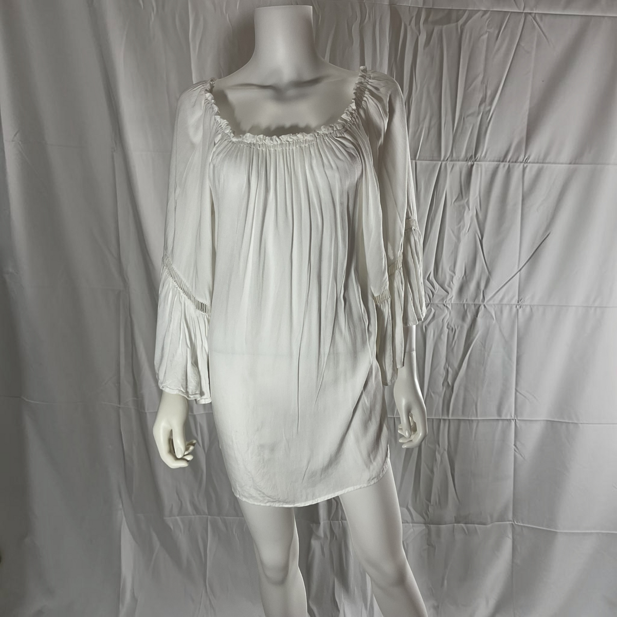A white long-sleeve slip dress or nightgown displayed on a mannequin against a wrinkled white fabric backdrop.