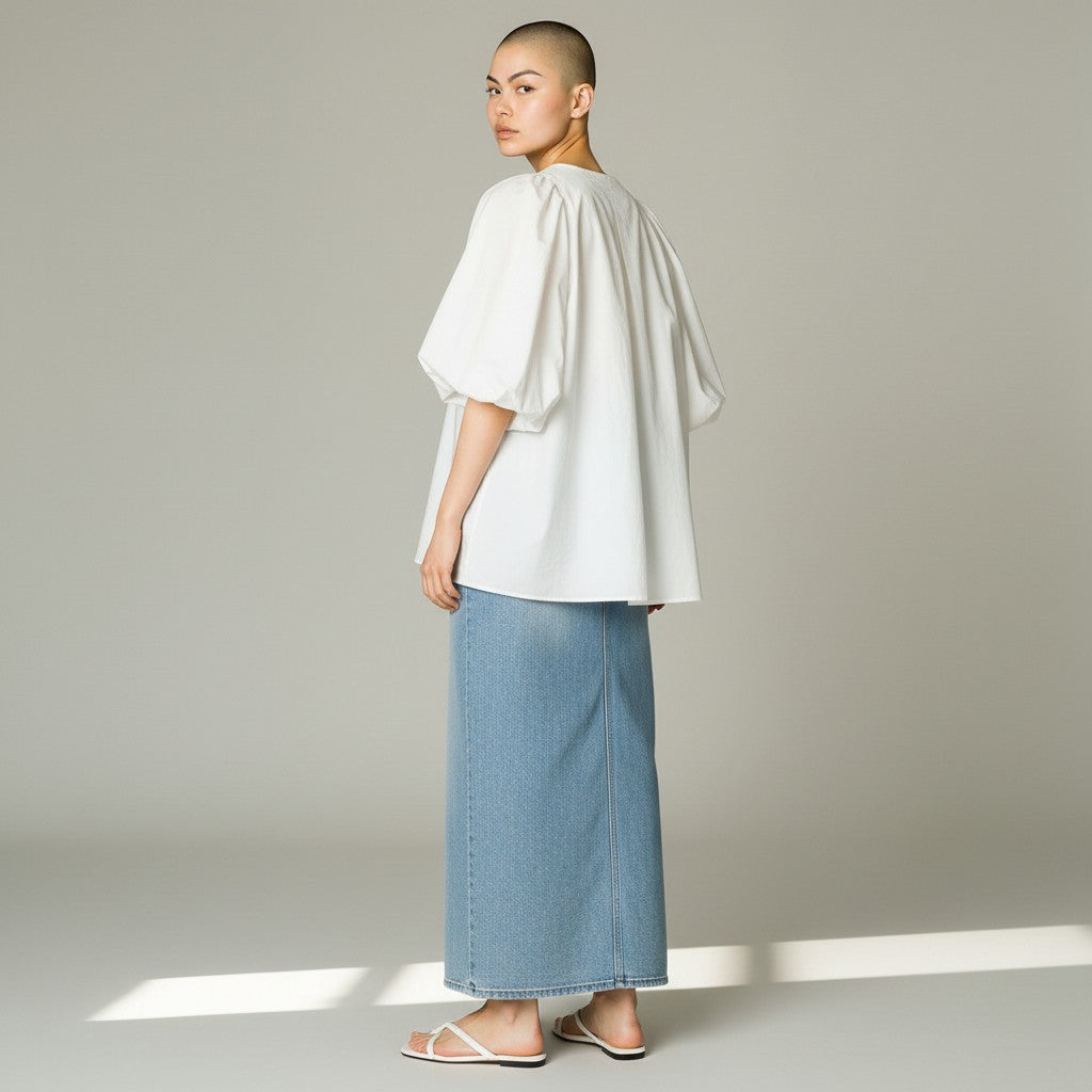 A model shown from the back wearing a white puff-sleeve blouse and a light blue wide-leg denim skirt, standing against a neutral gray studio background.