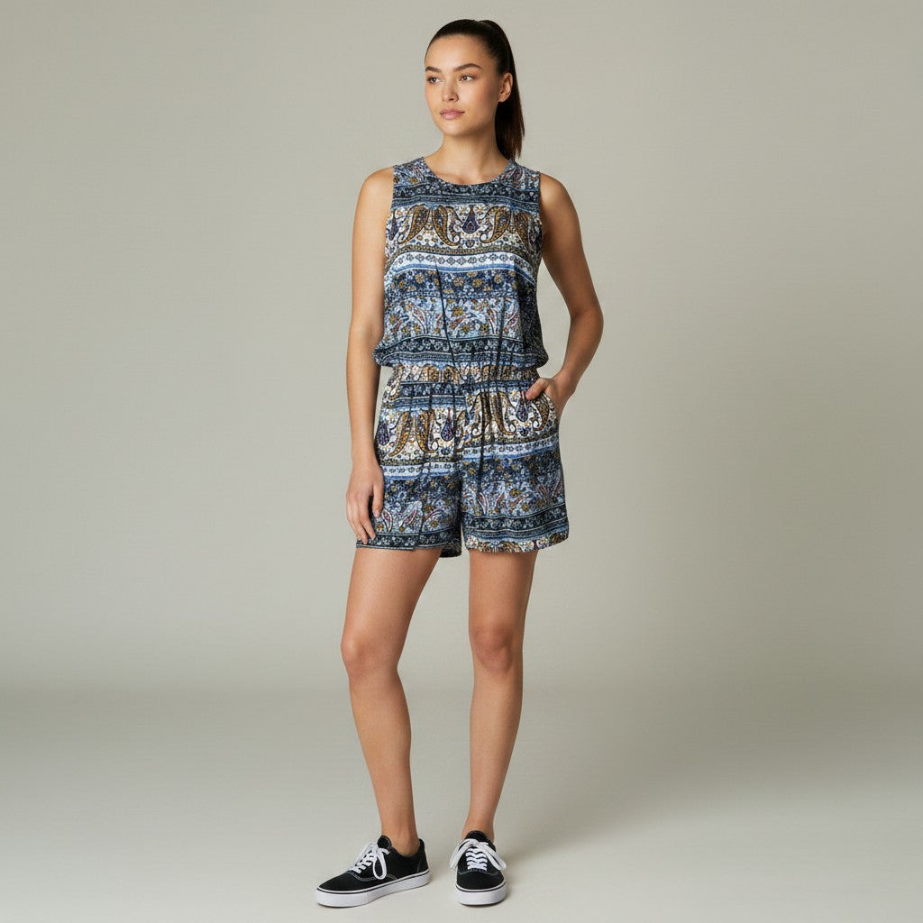A woman modeling a sleeveless matching top and shorts set with a detailed blue, brown, and beige paisley pattern, paired with black sneakers, against a neutral studio background.