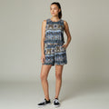 A woman modeling a sleeveless matching top and shorts set with a detailed blue, brown, and beige paisley pattern, paired with black sneakers, against a neutral studio background.