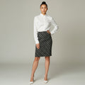 A woman modeling a white long-sleeve button-up shirt and a black knee-length skirt with a white geometric circle pattern, standing against a light gray studio background.
