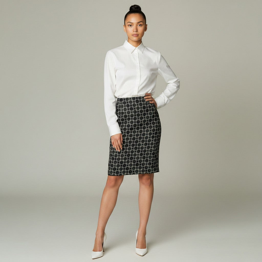A woman modeling a white long-sleeve button-up shirt and a black knee-length skirt with a white geometric circle pattern, standing against a light gray studio background.