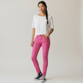 A woman modeling a white short-sleeve t-shirt and bright pink skinny jeans, standing against a light gray studio background.
