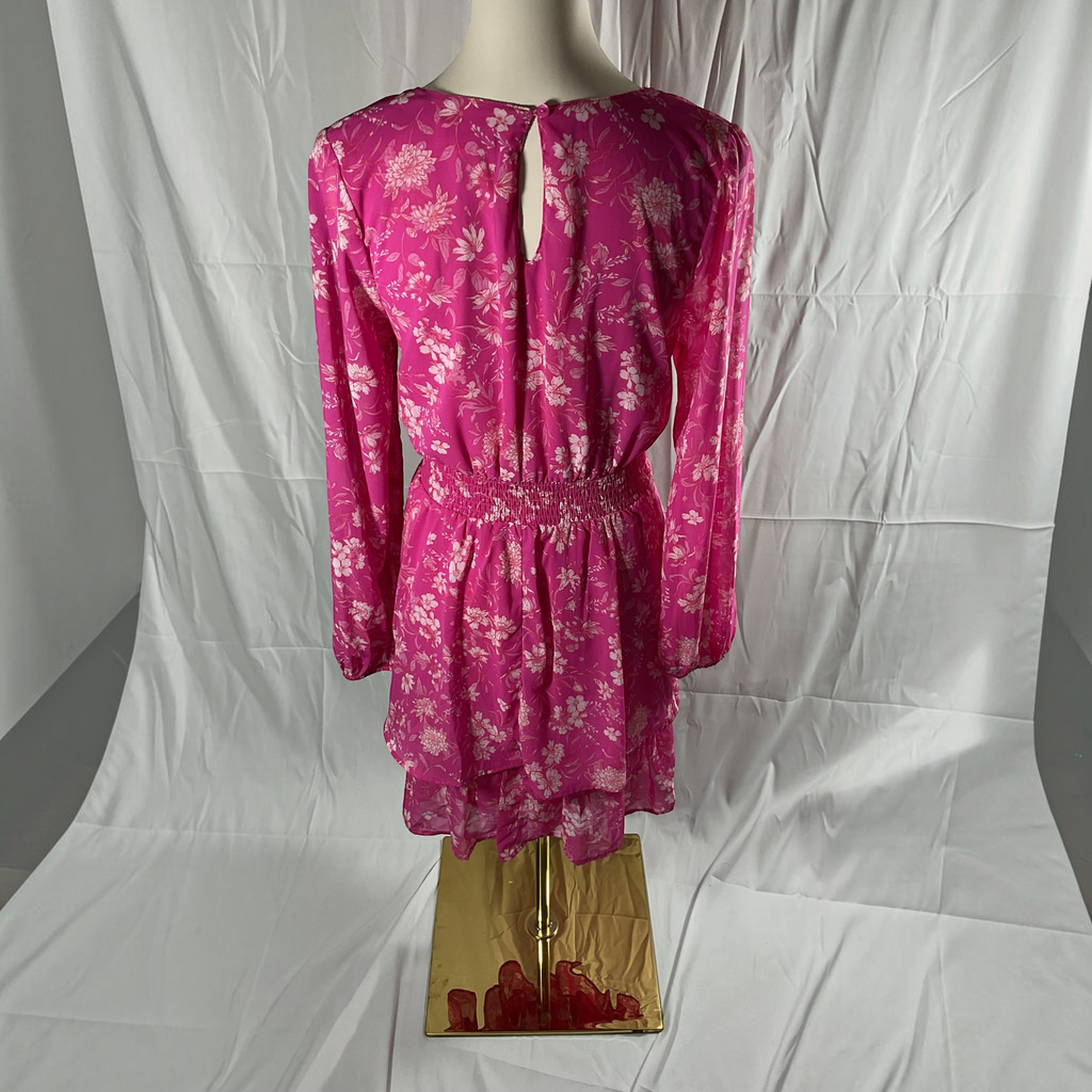 A pink long-sleeve mini dress with a white floral pattern, displayed on a mannequin torso against a wrinkled white fabric backdrop.