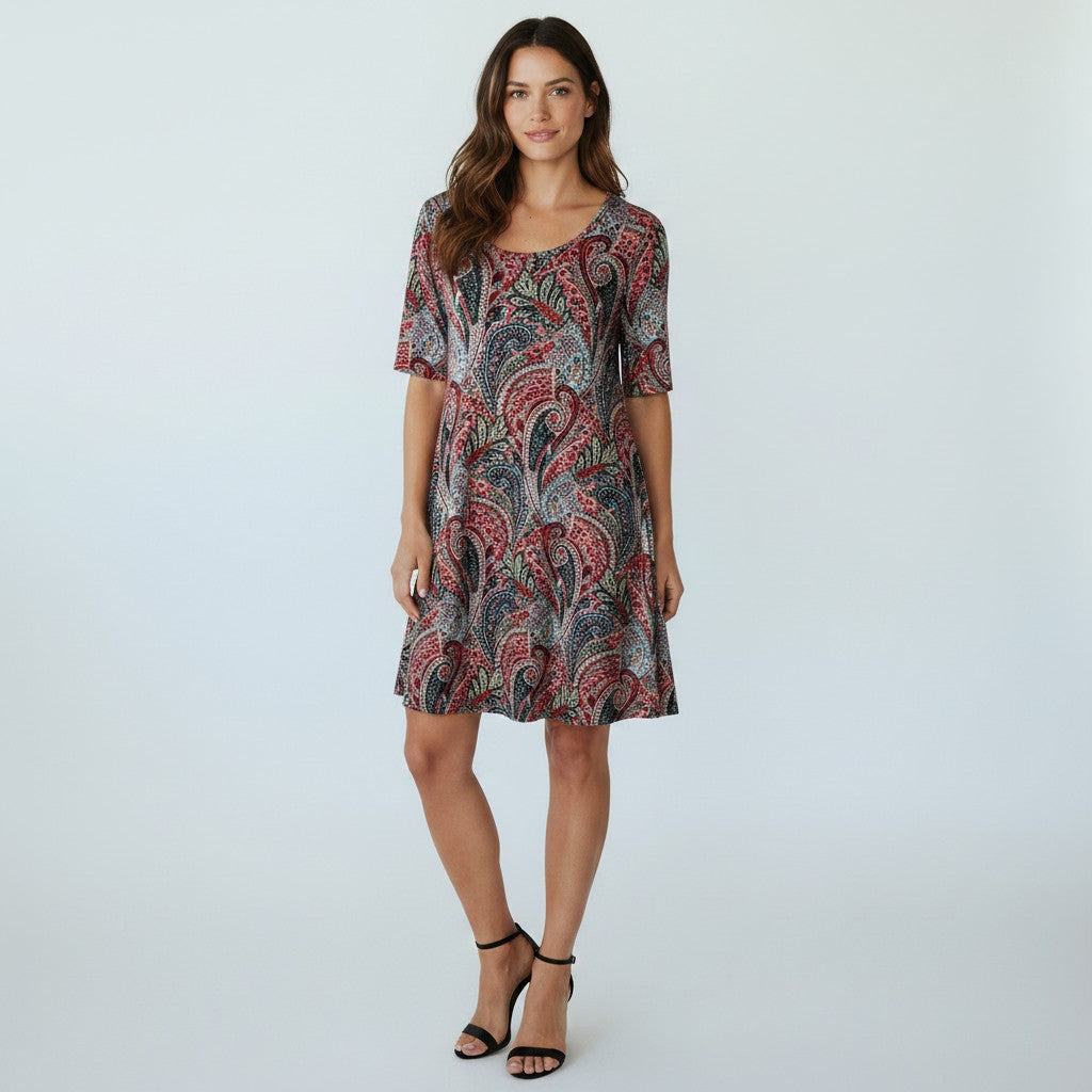 A woman modeling a short-sleeve knee-length dress with a red, black, and gray paisley pattern, standing against a light gray studio background.